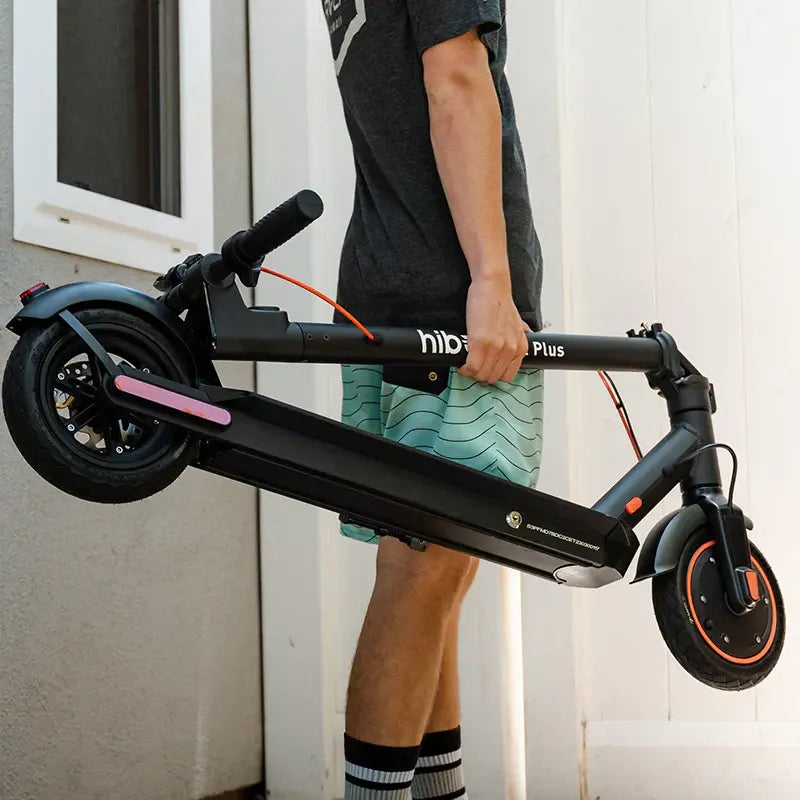 Person holding a folded electric scooter outdoors, portable commuter scooter design