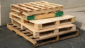 Stack of wooden shipping pallets outdoors on asphalt near a concrete wall