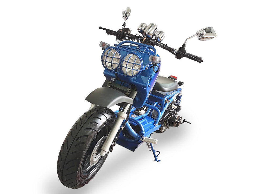 Blue motor scooter with dual round headlights and wide tires on white background
