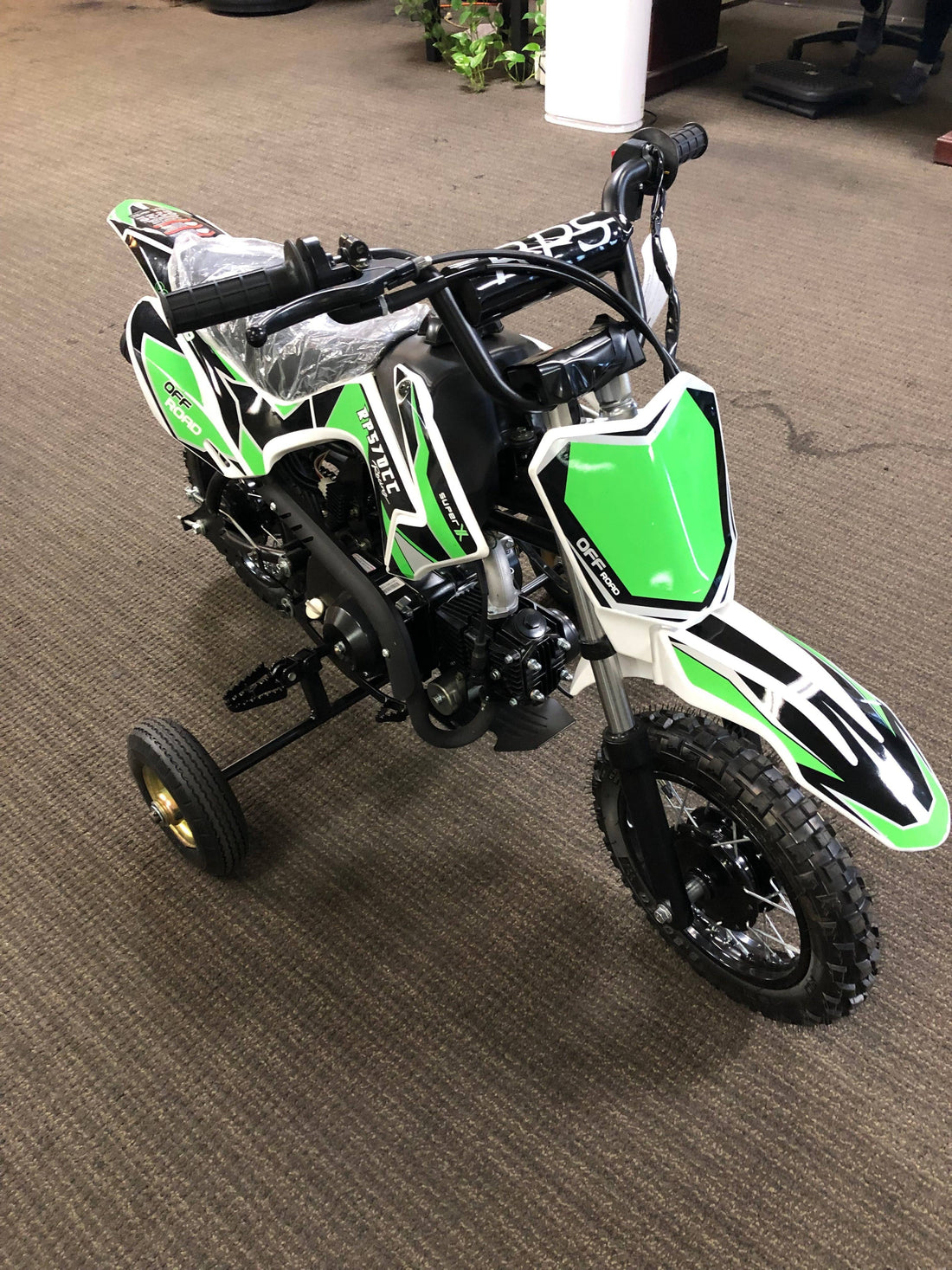 Green and black kids beginner dirt bike with training wheels on indoor carpet