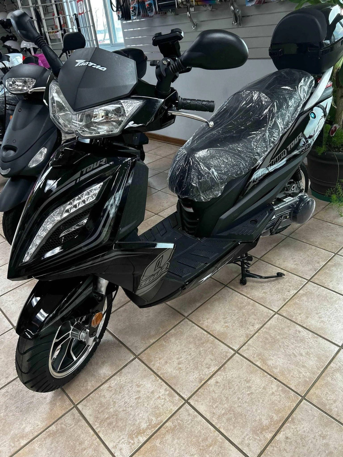 Black Tao Motor Phoenix 150 scooter on showroom tile floor, with plastic-wrapped seat
