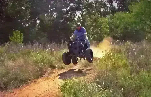 Person riding a four-wheeler ATV on a dirt trail in an outdoor, grassy area
