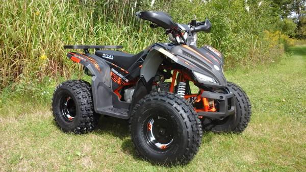 Black and orange 125cc youth ATV parked on grass, off-road, with rugged tires and sporty design