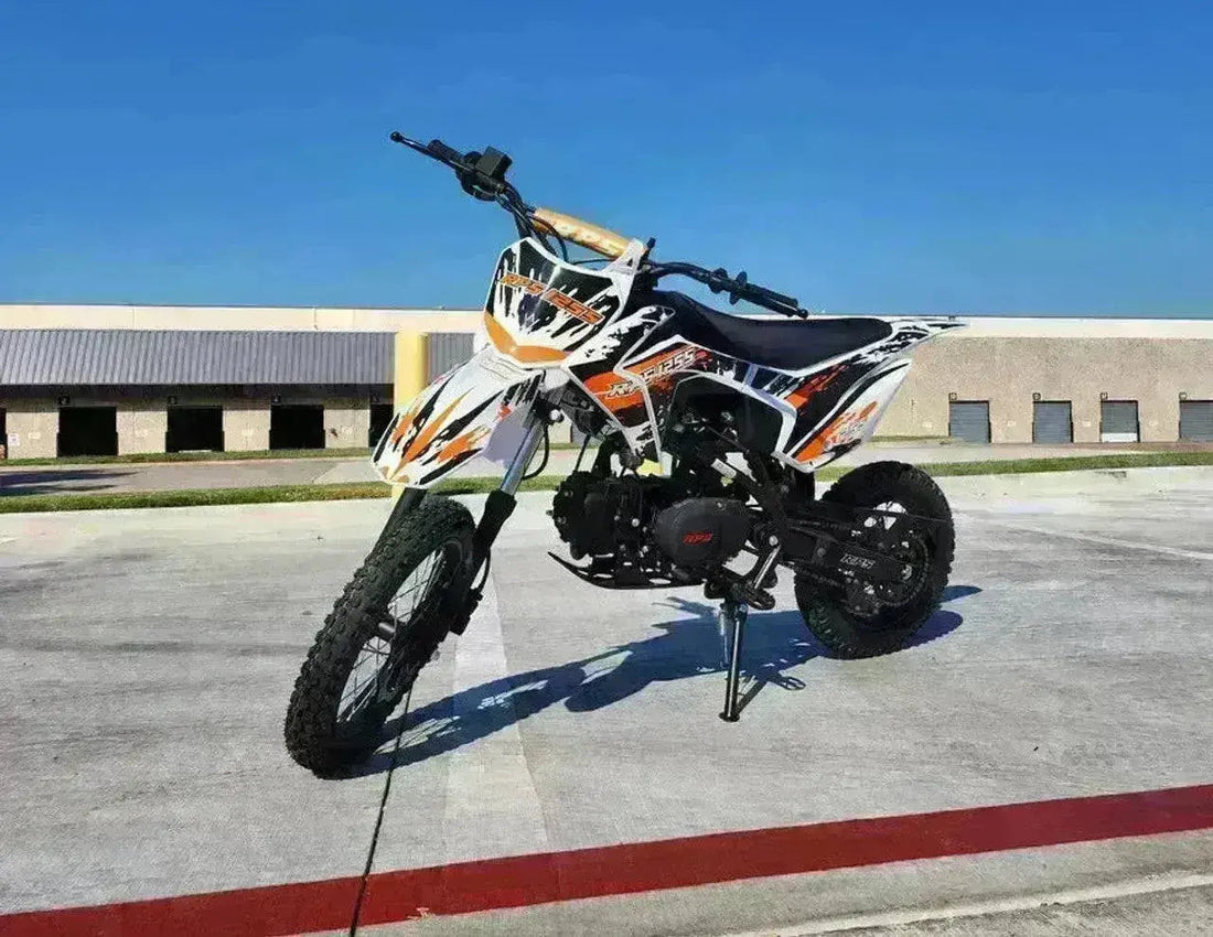 125cc youth dirt bike with orange and white graphics parked on pavement outdoors