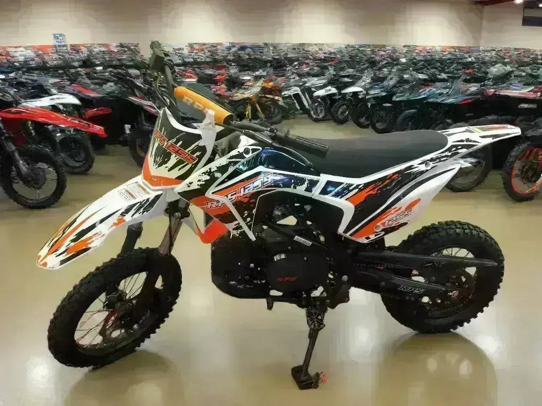 Youth 125cc dirt bike with orange, black, and white graphics in showroom, off-road motorcycle