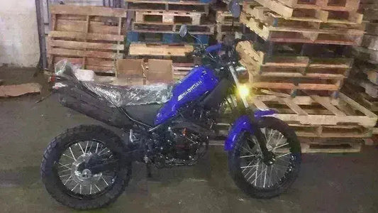 Blue 250cc enduro dirt bike with off-road tires parked indoors by wooden pallets