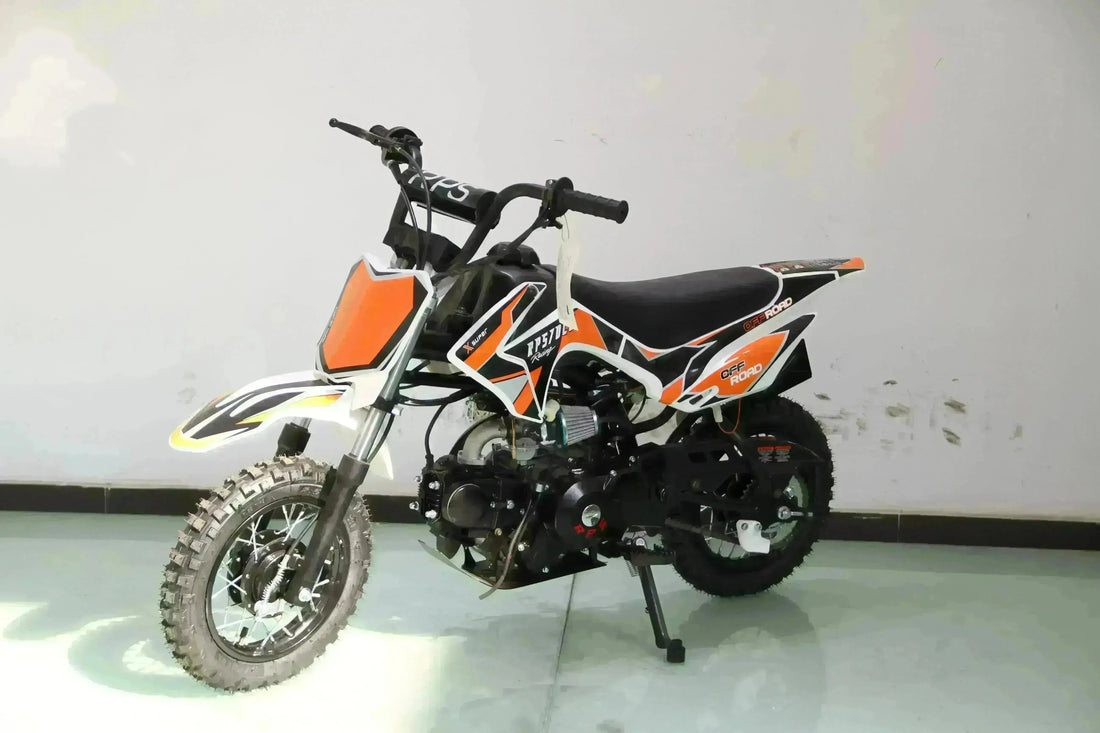 Small orange and black kids dirt bike with knobby tires and training wheels indoors