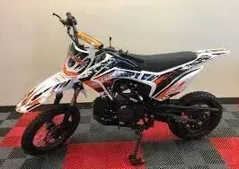 White and black RPS 125cc dirt bike with orange accents parked indoors on a checkered floor.