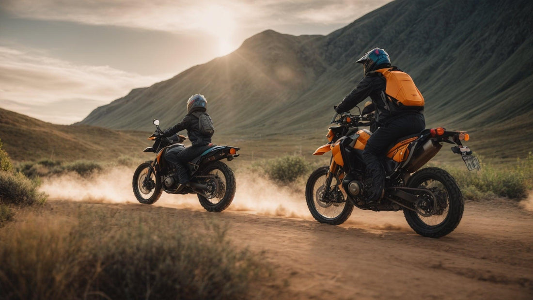 Two riders on orange dirt bikes trail riding in a scenic mountain landscape at sunset.
