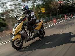 Rider in helmet on yellow motor scooter driving on road with blurred trees and traffic cones