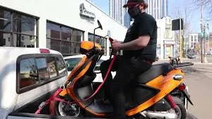 Man securing orange scooter in pickup truck bed for urban transport service