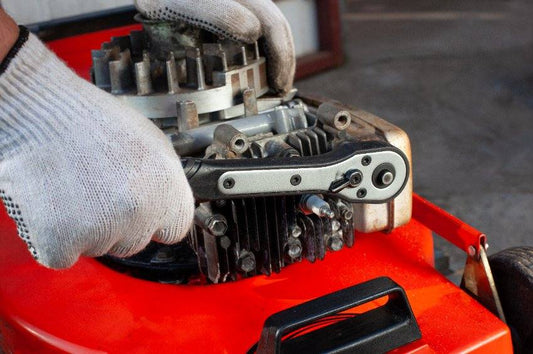 Technician in gloves repairing small engine with ratchet wrench on orange equipment