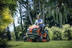 Person mowing lawn on orange riding lawn mower in a green, wooded yard