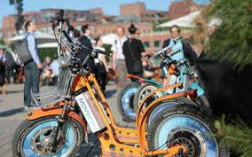 Electric scooters with wide tires parked outdoors in an urban setting with people nearby