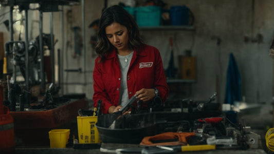 Woman in red mechanic jacket cleaning tools in a garage workshop with workbench and equipment