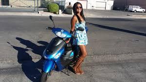 Woman standing next to a blue scooter on a sunny street, affordable scooter repair theme
