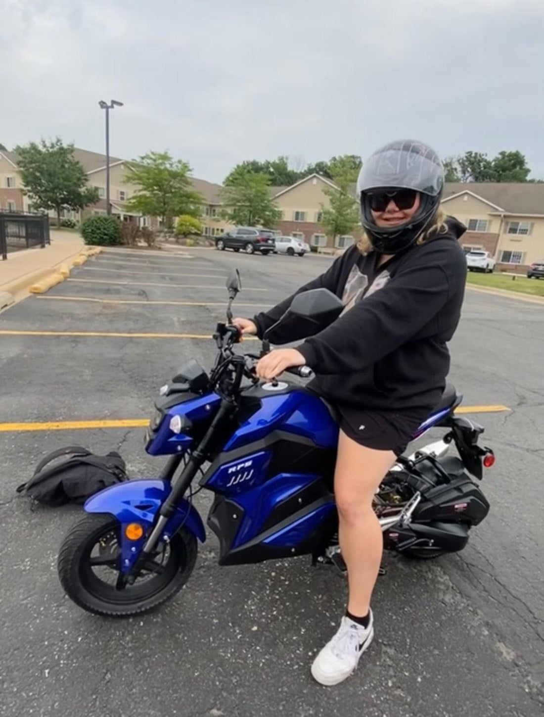 Rider wearing helmet on blue 150cc automatic motorcycle in parking lot, ideal for beginners