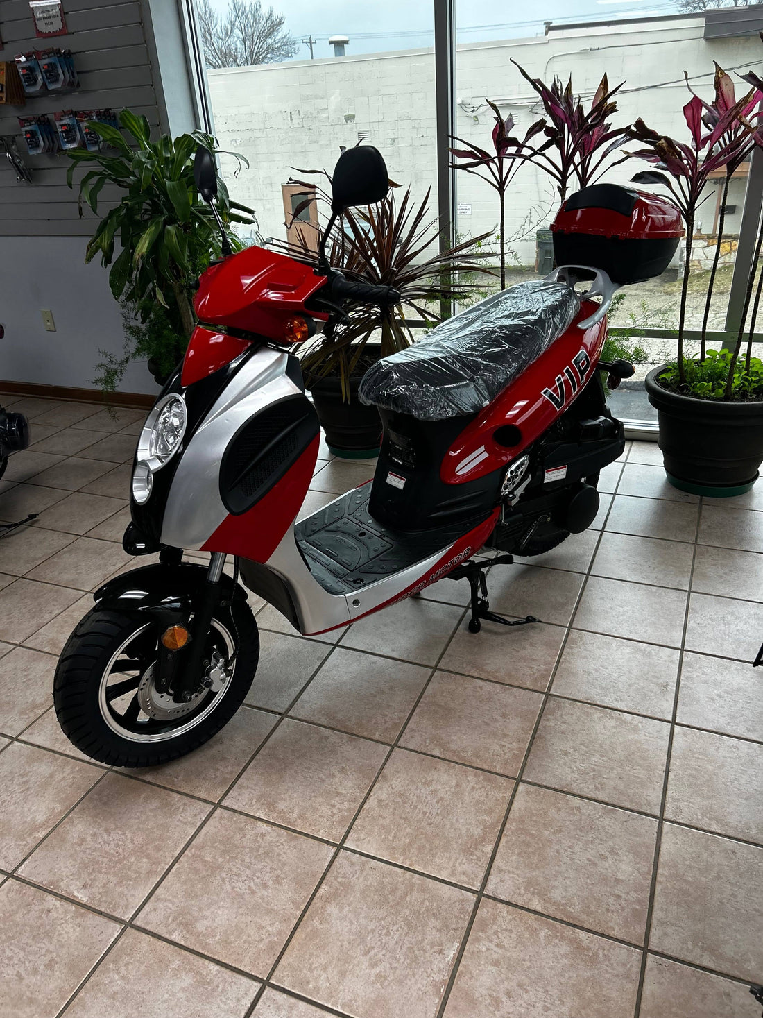 Red and silver 150cc motor scooter on showroom floor with plants in the background