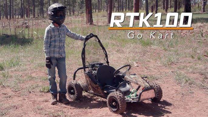 Child in helmet stands beside RTK100 kids go-kart in an outdoor off-road setting