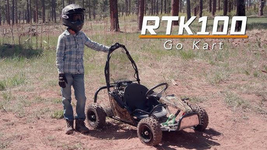 Child in helmet stands beside RTK100 kids go-kart in an outdoor off-road setting