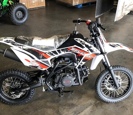 125cc dirt bike with knobby tires and sporty graphics, parked indoors on concrete