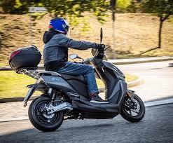 Person riding used motor scooter on road, wearing a helmet, with storage box attached