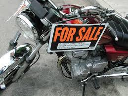 Used motorcycle with a visible 'For Sale' sign parked on pavement.