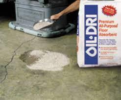 Person spreading Oil-Dri floor absorbent on garage oil spill, concrete surface cleanup