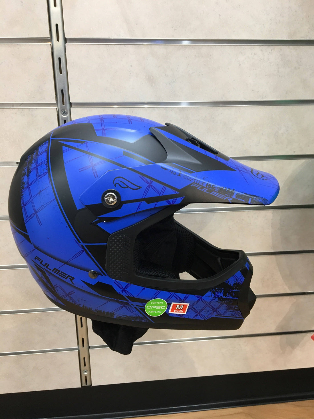 Blue youth ATV helmet with graphic design, full face protection, on display wall.