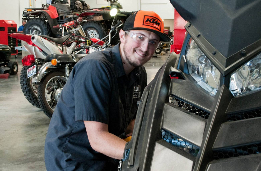 ATV mechanic in workshop servicing power sports vehicle with dirt bikes and ATVs in background