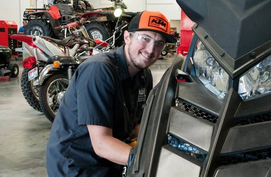 ATV mechanic in workshop servicing power sports vehicle with dirt bikes and ATVs in background