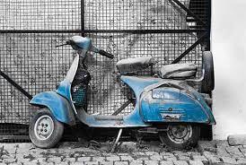 Weathered blue scooter parked on stone pavement in front of metal gate, powersports vehicle