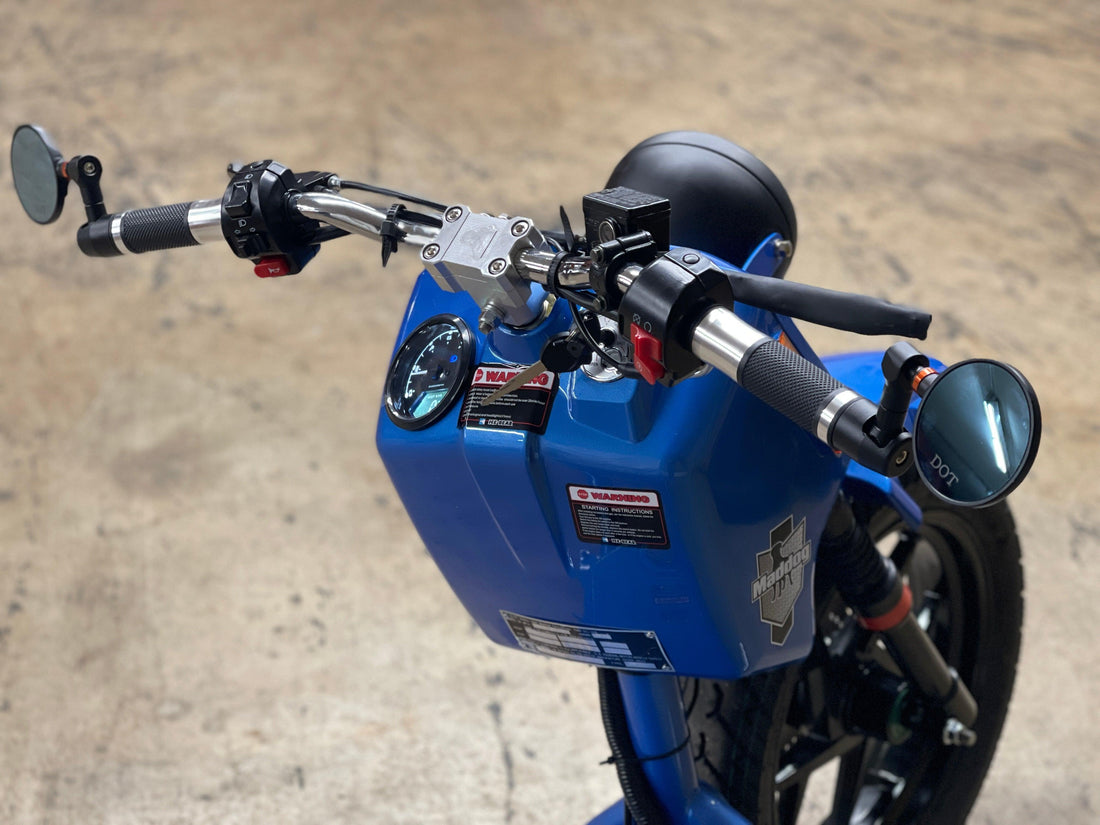 Close-up of blue Maddog 150cc scooter handlebars and mirrors on concrete floor