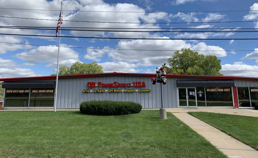 Exterior of a dealership with ATVs, go-karts, dirt bikes, mopeds, and scooters signage, scooter display on pole
