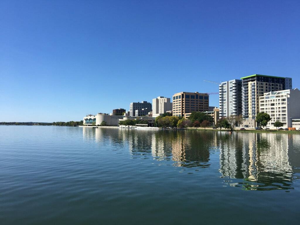City buildings skyline reflected on the calm lake water under blue sky on a clear day