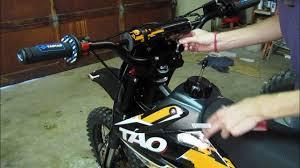 Person adjusting handlebars on a Taotao dirt bike in a garage setting