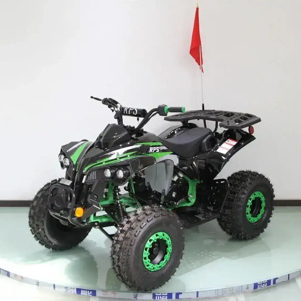 Black and green all-terrain ATV with off-road tires and a rear cargo rack indoors